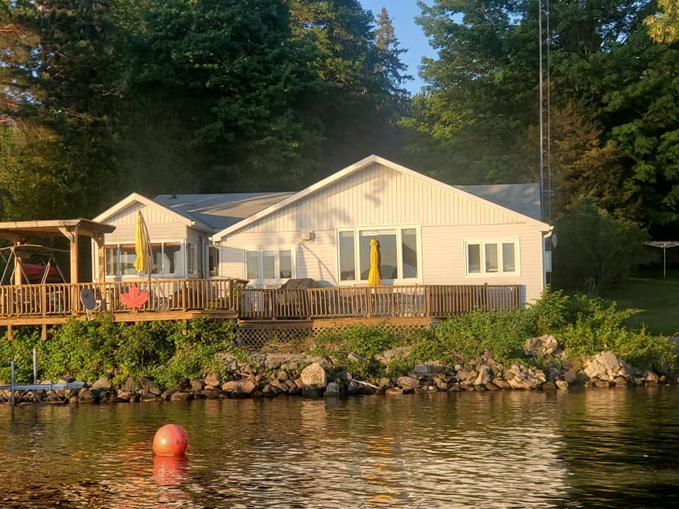 Lakefront cottage photographed from the water with a broad deck and replacement windows