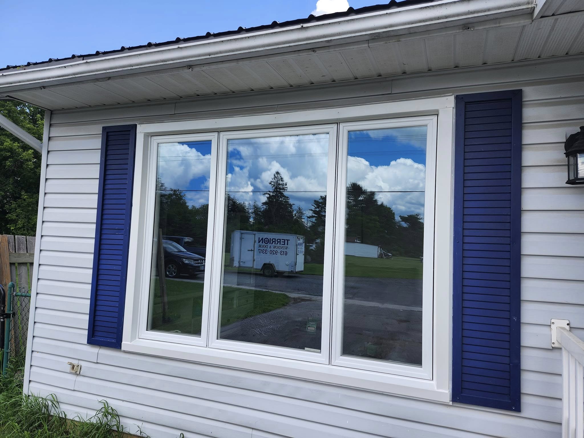Wide exterior window with clean white trim capping and dark blue shutters on a siding-clad home